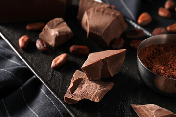 Pieces of tasty milk chocolate, cocoa beans and powder on table, closeup