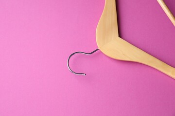 Empty wooden hanger on bright pink background, top view. Space for text