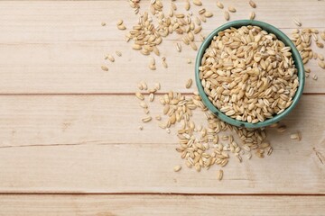 Dry pearl barley in bowl on light wooden table, top view. Space for text