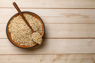 Dry pearl barley in bowl and spoon on light wooden table, top view. Space for text