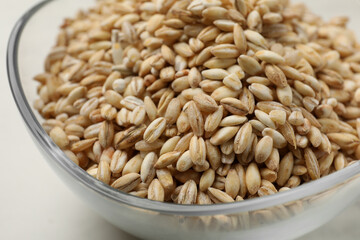Dry pearl barley in bowl on white table, closeup