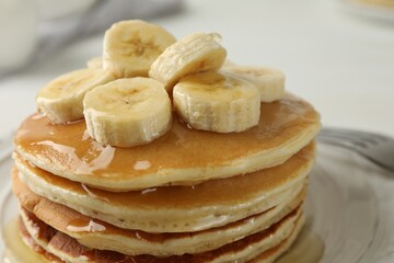 Delicious pancakes with bananas and honey on white table, closeup