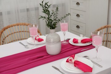 Table setting. Glasses of tasty beverage, plates, pink napkins and vase with green branches in dining room