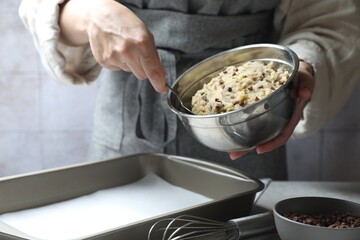 Woman making chocolate chip cookie dough at table, closeup