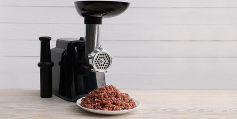 Electric meat grinder and beef mince on light wooden table. Banner design with space for text