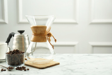 Glass chemex coffeemaker, kettle and beans on white marble table, space for text