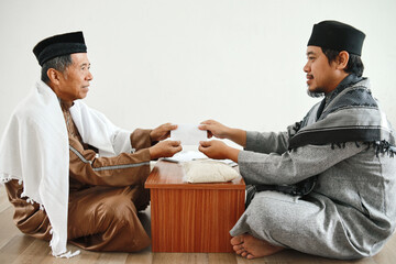 Side view muslim man giving envelope  filled with money to mosque administrator for zakat or...