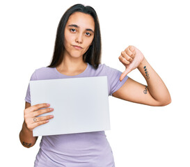 Young hispanic woman holding blank empty banner with angry face, negative sign showing dislike with...