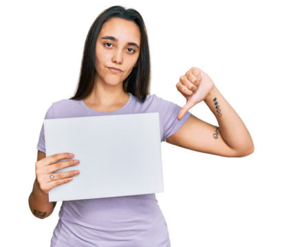 Young hispanic woman holding blank empty banner with angry face, negative sign showing dislike with thumbs down, rejection concept
