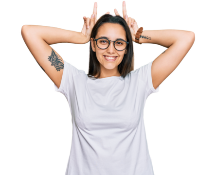 Young hispanic woman wearing casual white t shirt posing funny and crazy with fingers on head as bunny ears, smiling cheerful