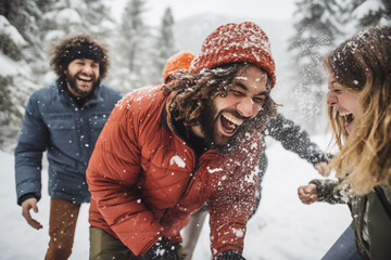 Man wearing warm winter clothes laughs and smiles while getting hit by a snowball from his group of friends