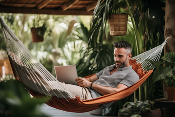 Man working remotely on a laptop while relaxing in a hammock from a tropical destination