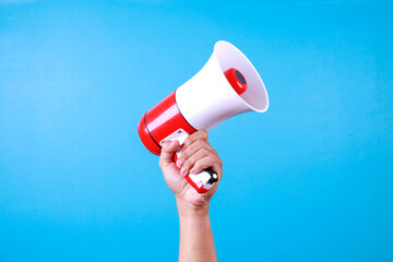 Close up hand holding megaphone over isolated blue background.