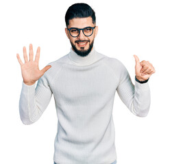 Young arab man with beard wearing elegant turtleneck sweater and glasses showing and pointing up with fingers number six while smiling confident and happy.