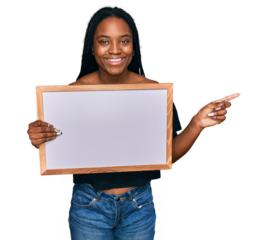 Young african american woman holding empty white chalkboard smiling happy pointing with hand and finger to the side