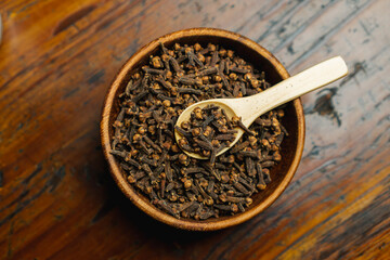 wooden bowl and spoon full of clove on top of wooden table, concept of using spice in kitchen