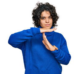 Young hispanic woman with curly hair wearing turtleneck sweater doing time out gesture with hands,...