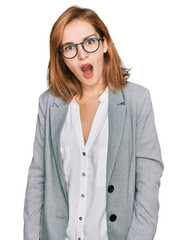 Young caucasian woman wearing business style and glasses in shock face, looking skeptical and sarcastic, surprised with open mouth