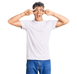 Fototapeta premium Young handsome man wearing casual white tshirt doing peace symbol with fingers over face, smiling cheerful showing victory