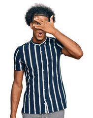 Fototapeta na wymiar African american man with afro hair wearing casual clothes peeking in shock covering face and eyes with hand, looking through fingers with embarrassed expression.