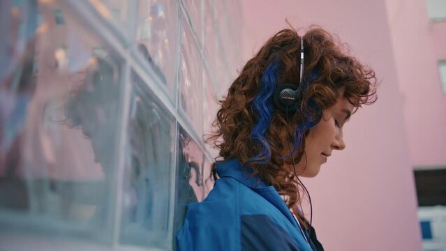 Headphones woman feeling calmness listening music on street close up. Curly girl