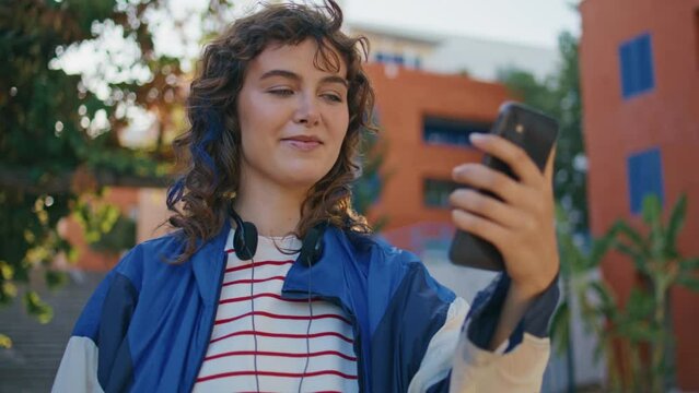 Trendy girl video calling by smartphone at urban street close up. Woman talking