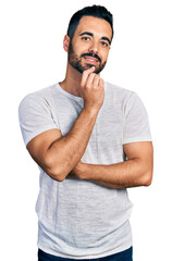 Young hispanic man with beard wearing casual grey t shirt smiling looking confident at the camera with crossed arms and hand on chin. thinking positive.