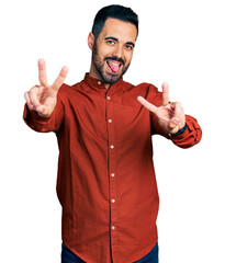 Young hispanic man with beard wearing casual shirt smiling with tongue out showing fingers of both...
