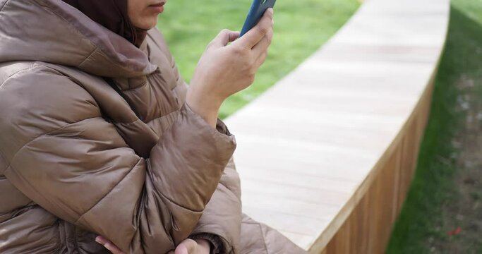 women hand holding smart phone sitting on park bench 