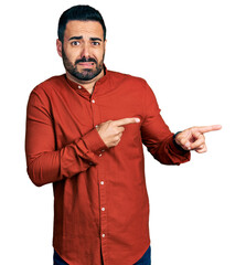 Young hispanic man with beard wearing casual shirt pointing aside worried and nervous with both...