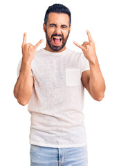 Young hispanic man wearing casual clothes shouting with crazy expression doing rock symbol with hands up. music star. heavy concept.