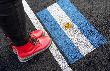 a womman with a boots standing on asphalt next to flag of Argentina and border
