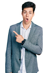Young hispanic man wearing business clothes surprised pointing with finger to the side, open mouth...