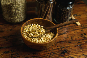 coriander seeds on a wooden bowl, with a spice jar beside it, concept of using a natural spice on a kitchen