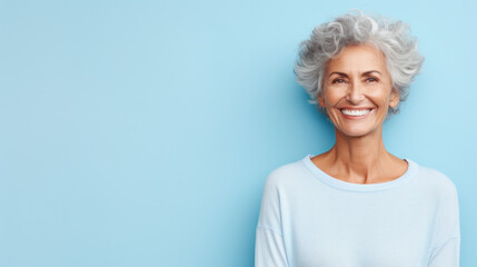 Closeup face of senior business woman standing against blue background with copy space. Portrait of successful woman in blue shirt feeling confident and looking at camera. Happy mature woman face.