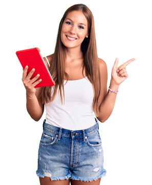 Young beautiful hispanic woman holding touchpad smiling happy pointing with hand and finger to the side