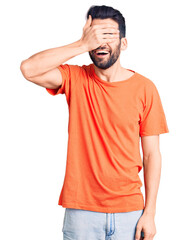 Fototapeta premium Young handsome man with beard wearing casual t-shirt smiling and laughing with hand on face covering eyes for surprise. blind concept.