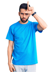 Naklejka premium Young handsome man with beard wearing casual t-shirt making fun of people with fingers on forehead doing loser gesture mocking and insulting.