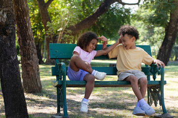Young sister and her older brother sitting on a bench enjoyed teasing each other on  bright summer...