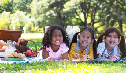 Three little girls lying together on picnic blanket, have fun drawing on paper together on a bright...