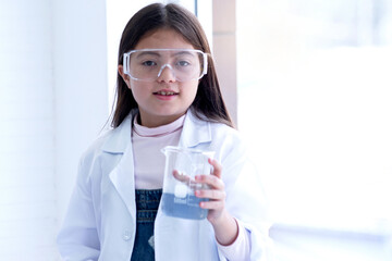 Caucasian student girl in lab coat showing chemical liquid in glass beaker, students working in the laboratory
