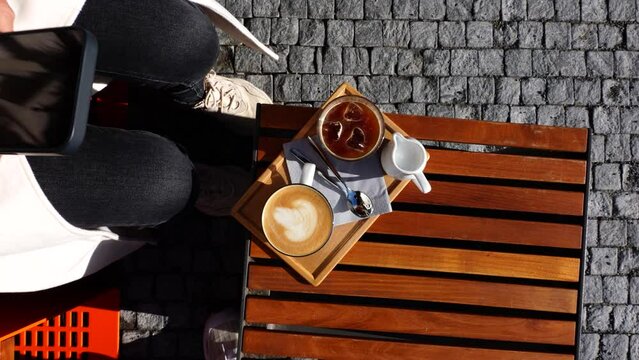 Ice coffee and latte cup on wooden outdoor table while girl take a photo