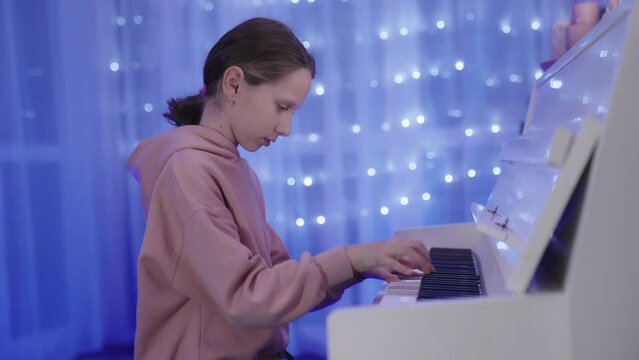 Talented pretty little girl plays white Piano with temperament. Live music scene with bright blurred bokeh.