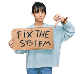 Young hispanic woman holding fix the system banner cardboard with angry face, negative sign showing...