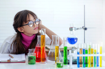 Female student with test glasses liquid on table in laboratory, thinking or planning something in...