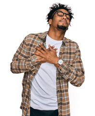 Young african american man with beard wearing casual clothes and glasses smiling with hands on chest with closed eyes and grateful gesture on face. health concept.