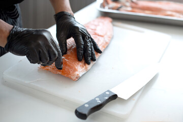 Close up, Japanese chef's hands uses tweezers to remove fish bones from fresh salmon on a cutting board, steps for preparing ingredients for Japanese cooking - obrazy, fototapety, plakaty