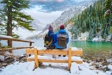 Lake Agnes by Lake Louise Banff National Park with snowy mountains in the Canadian Rocky Mountains during winter. A couple of men and women sitting on a bench by the emerald green lake in Canada with - obrazy, fototapety, plakaty