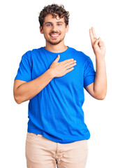 Young handsome man with curly hair wearing casual clothes smiling swearing with hand on chest and...