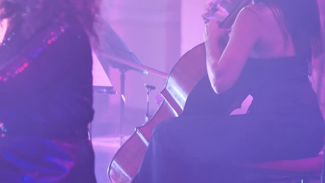 Woman cellist playing a parry on stage with bright lights and smoke show. Close-up of the instrument and the girl's hands. Professional musician playing as part of an orchestra
